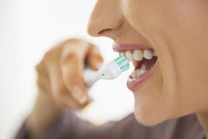 A woman is brushing her teeth with an electric toothbrush.